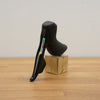 A black SRAM shift lever displayed on a small wooden block on a light wood tabletop against a plain light gray wall.