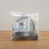 A clear plastic bag containing a black coiled cable or hose with a small red-and-white tag, placed on a light wood surface against a plain light gray wall.