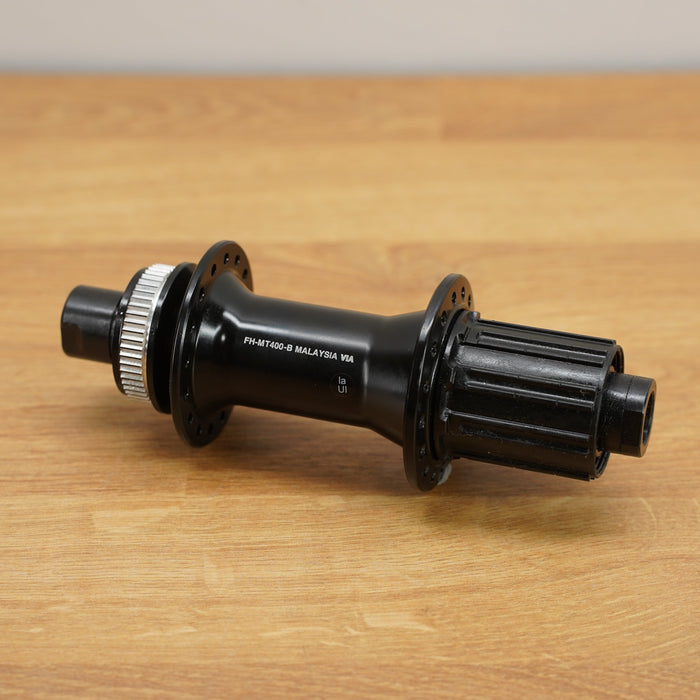 A black bicycle hub with a silver splined end and white printed text, resting on a light brown wooden tabletop.