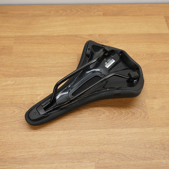A black bicycle saddle photographed from above on a light brown wooden floor.