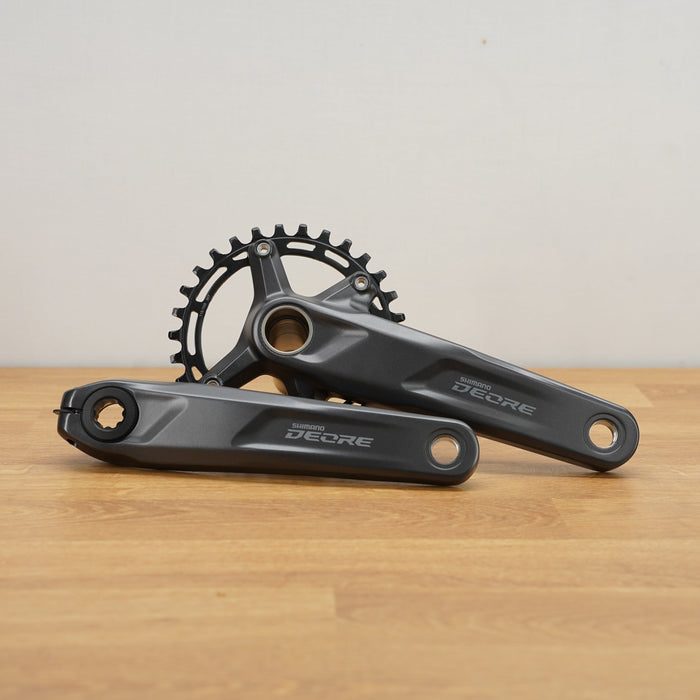A pair of black Decore bicycle cranksets resting on a light wood surface against a neutral off-white background.