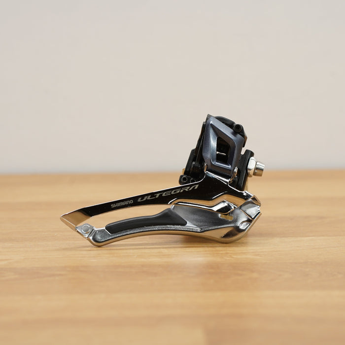 A Shimano Ultegra bicycle derailleur in black and silver, resting on a light wooden tabletop against a neutral beige background.