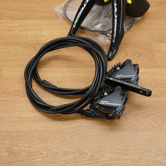 A Shimano hydraulic disc brake cable assembly with a coiled black cable and black brake lever, placed on a light brown wooden surface.