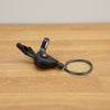 A black Shimano bicycle shift lever with an attached cable resting on a light brown wooden floor against a neutral beige wall.