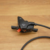 A black bicycle caliper with a black cable, resting on a light brown wooden surface.