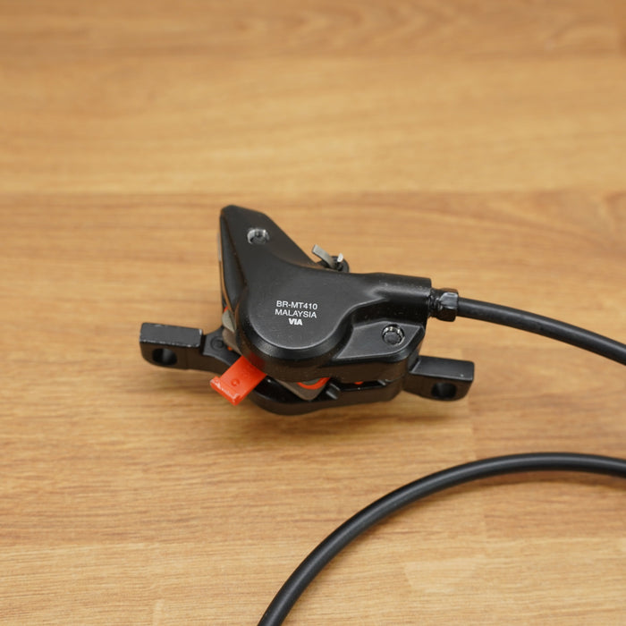 A black bicycle caliper with a black cable, resting on a light brown wooden surface.