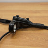 A black bicycle brake lever with attached cables, resting on a light brown wooden surface.