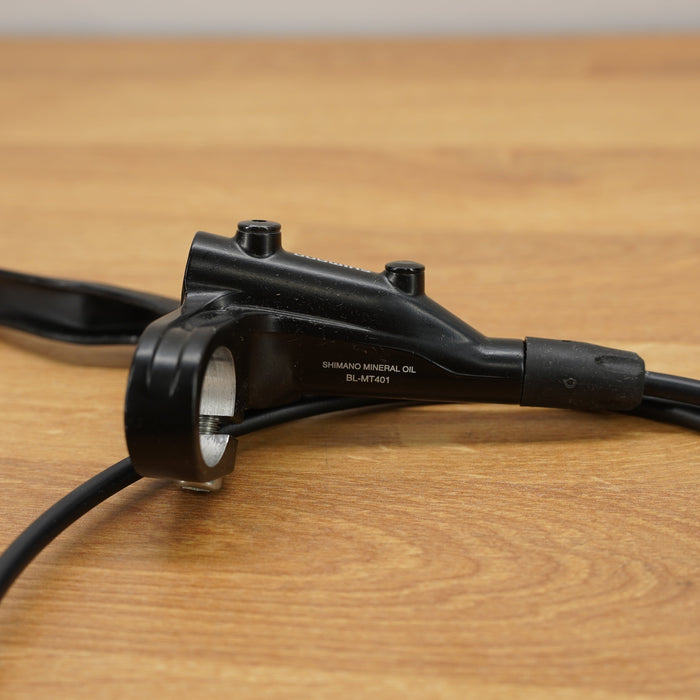 A black bicycle brake lever with attached cables, resting on a light brown wooden surface.