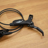 A Shimano SRAM bicycle brake lever and matching brake caliper with a coiled black cable, displayed on a light brown wooden surface.