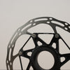 A close-up shot of a black bicycle disc brake rotor with a matching black metal hub, set against a plain light gray background.
