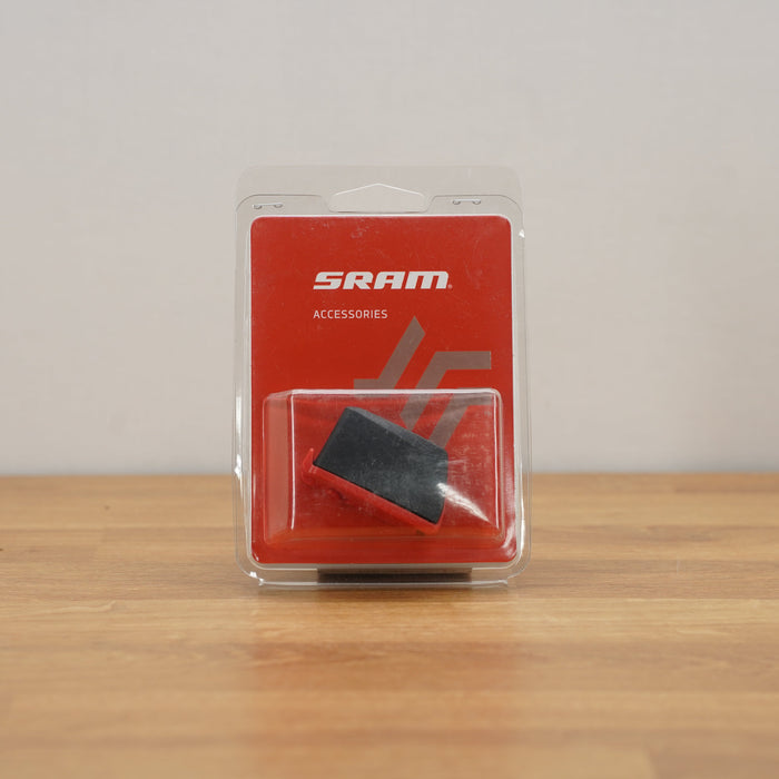 SRAM Accessories black and red component in clear plastic blister packaging, standing on a wooden surface against a light gray wall.