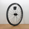 A carbon fiber ZIPP bicycle wheel with a black deep-section rim, thin black spokes, and a black hub, standing upright on a light wood floor against a plain white wall.