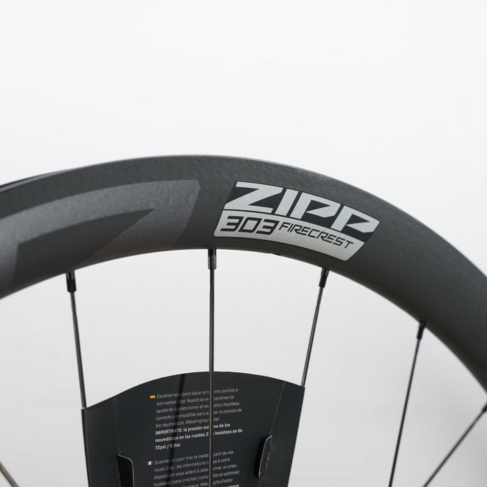Close-up of a dark gray Zipp 303 firecrest carbon fiber bicycle wheel rim with the brand logo clearly visible against a light gray background.