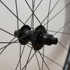 Close-up of a black bicycle hub with thin black spokes against a light neutral background.