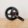 A black SRAM rival crankset with 2 chainrings sitting on a light brown wooden surface against a plain white background. 