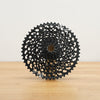 A black SRAM cassette photographed on a light wooden surface against a plain white wall.