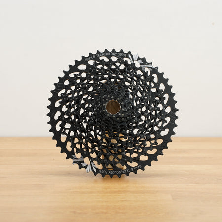 A black SRAM cassette photographed on a light wooden surface against a plain white wall.