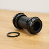 A black SRAM bottom bracket photographed on a light brown wooden surface against a plain white wall. 