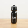 A black Peak Five Collective branded water bottle photographed on a light brown wooden surface against a plain white wall.