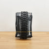 A black Maxxis Dissector tire photographed on a light brown wooden surface against a plain white wall. 