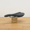 A black WTB bicycle saddle with white details, displayed on a small wooden block stand on a light wood tabletop against a neutral wall.