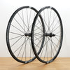 Two black DT Swiss aluminum road bicycle wheels standing upright on a light wood surface against a plain white wall.