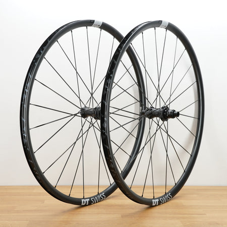 Two black DT Swiss aluminum road bicycle wheels standing upright on a light wood surface against a plain white wall.