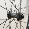 Close-up of a black DT Swiss wheel hub mounted on a bicycle wheel, with thin black spokes and part of the tire visible against a light neutral background.