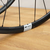 Close-up of a black DT Swiss E1800 road bike wheel with thin black spokes, resting on a light wood surface.