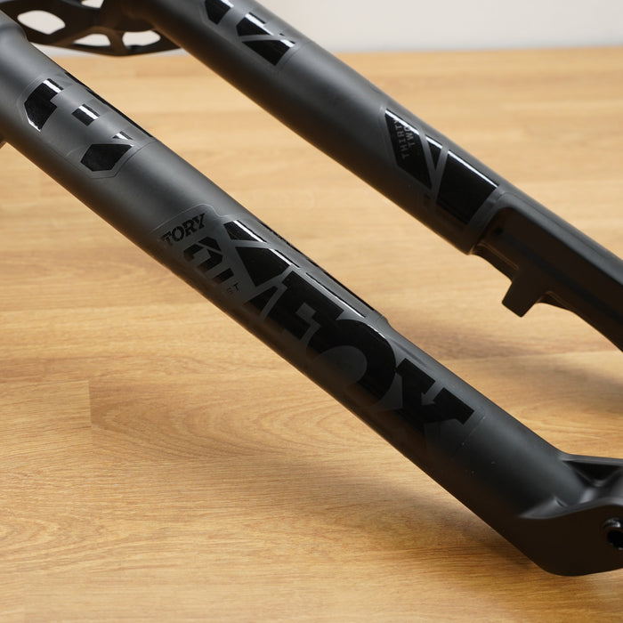 Close-up of a black Fox mountain bike front fork, resting on a light wood floor.