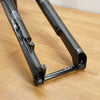 A black Fox mountain bike fork resting on a light wood floor, showing the front triangle and suspension components.