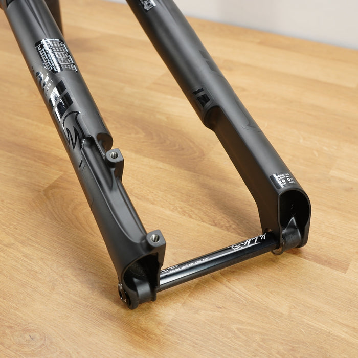 A black Fox mountain bike fork resting on a light wood floor, showing the front triangle and suspension components.