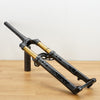 A black and gold mountain bike front suspension fork displayed on a wooden table against a plain white wall.