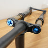 A close-up of a black bicycle front fork with gold-colored stanchions and bright blue anodized top caps, resting on a wooden surface against a plain wall.