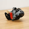 A grey and black SRAM bicycle rear derailleur with a red battery cover photographed on a light brown wooden surface against a plain white background.