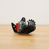 A grey and black SRAM bicycle rear derailleur with a red battery cover photographed on a light brown wooden surface against a plain white background.
