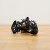 A black SRAM rear derailleur component with visible SRAM branding, resting on a light wood surface against a plain off-white background.