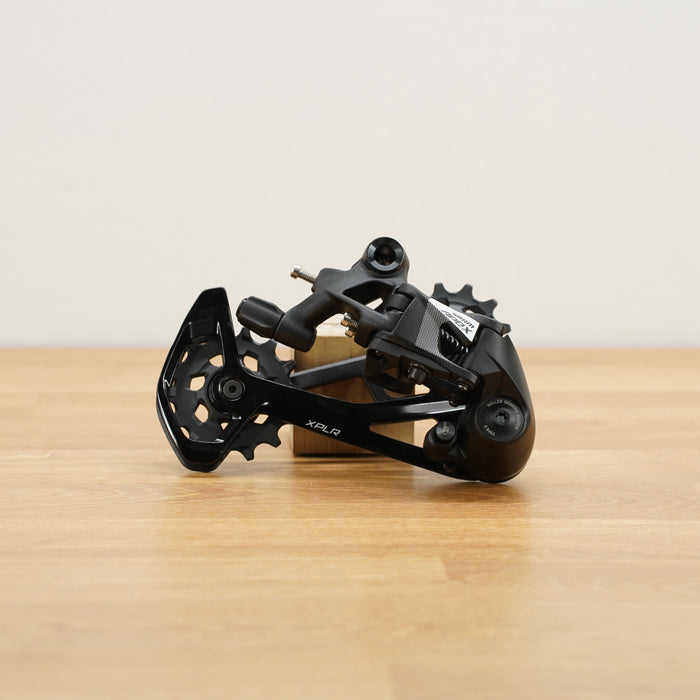 A black SRAM rear derailleur component with visible SRAM branding, resting on a light wood surface against a plain off-white background.