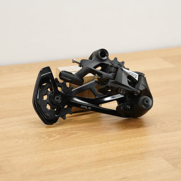 A black SRAM rear derailleur component with visible SRAM branding, resting on a light wood surface against a plain off-white background.