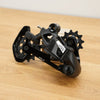 A black SRAM rear derailleur component with visible SRAM branding, resting on a light wood surface against a plain off-white background.