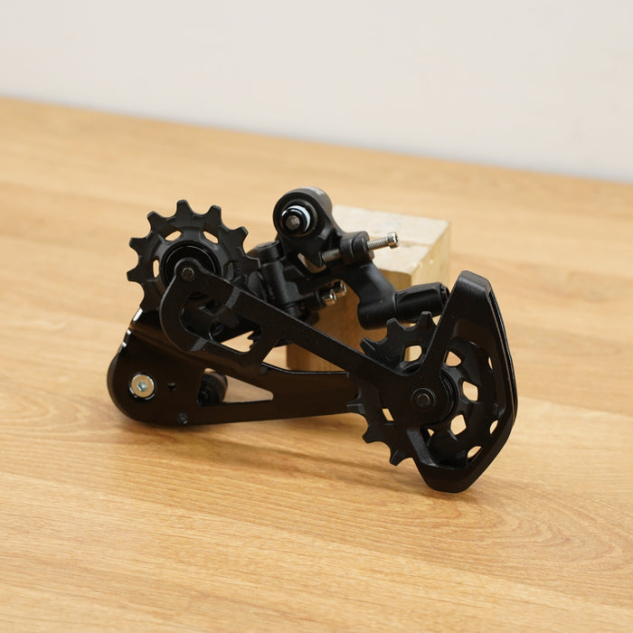 A black SRAM rear derailleur component with visible SRAM branding, resting on a light wood surface against a plain off-white background.