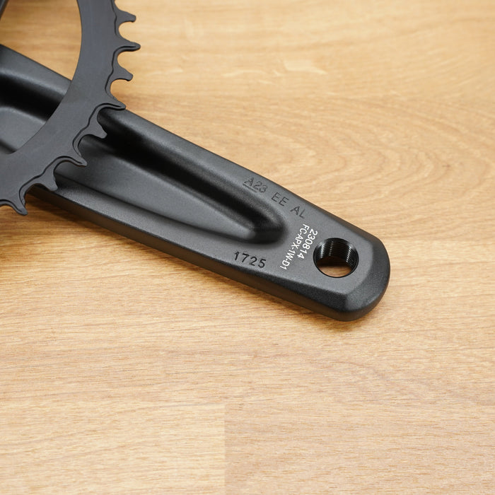 A close-up of a black crank arm and chainring from a SRAM bicycle crankset, resting on a light wood grain surface.