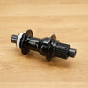A black bicycle hub with a silver splined end, resting on a light brown wooden surface.