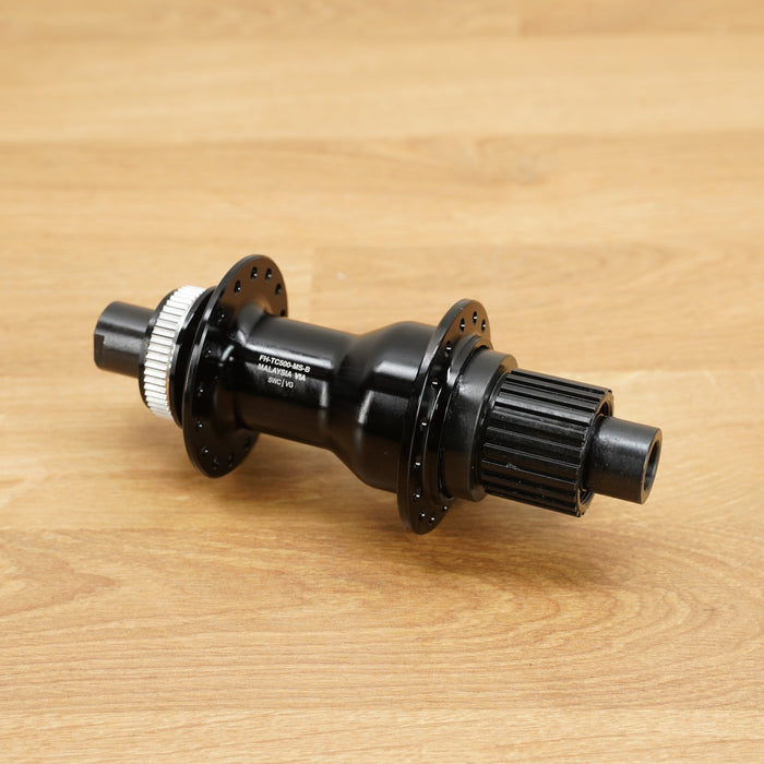 A black bicycle hub with a silver splined end, resting on a light brown wooden surface.