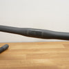 A matte black drop handlebar resting on a light wood tabletop against a plain off-white wall.