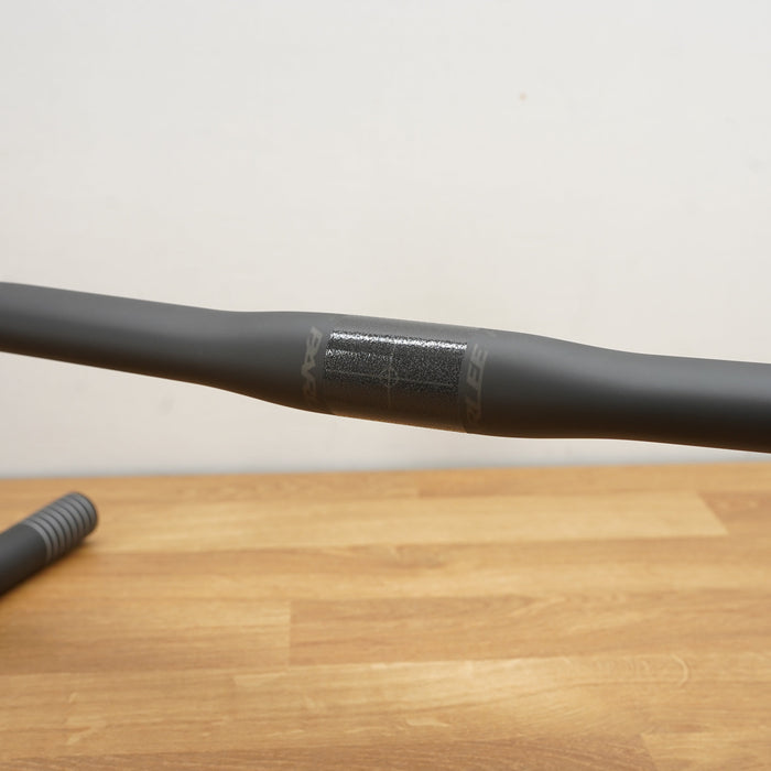 A matte black drop handlebar resting on a light wood tabletop against a plain off-white wall.
