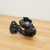 A black and dark gray Shimano GRX bicycle rear derailleur resting on a light wood tabletop against a plain off-white wall.