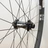 Close-up of a bicycle wheel hub and spokes with a dark gray rim against a plain light background.