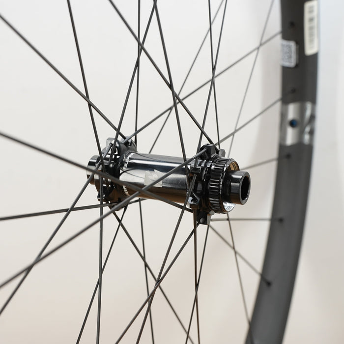 Close-up of a bicycle wheel hub and spokes with a dark gray rim against a plain light background.